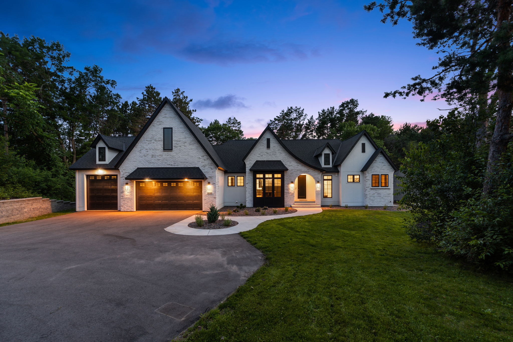 Modern Tudor home exterior at dusk with three-car garage and wooded lot