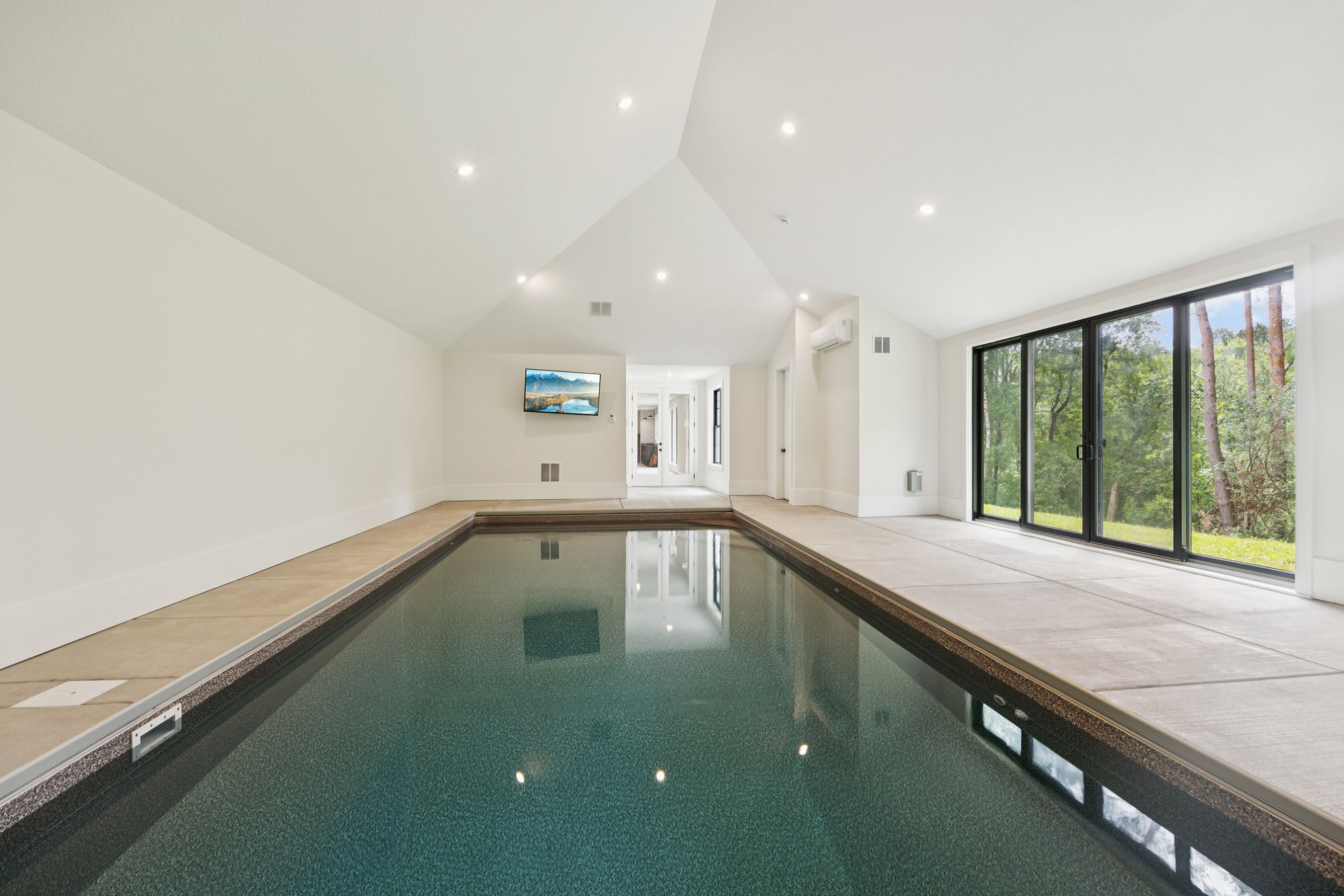 Indoor pool room with vaulted ceiling and wall of windows to the woods
