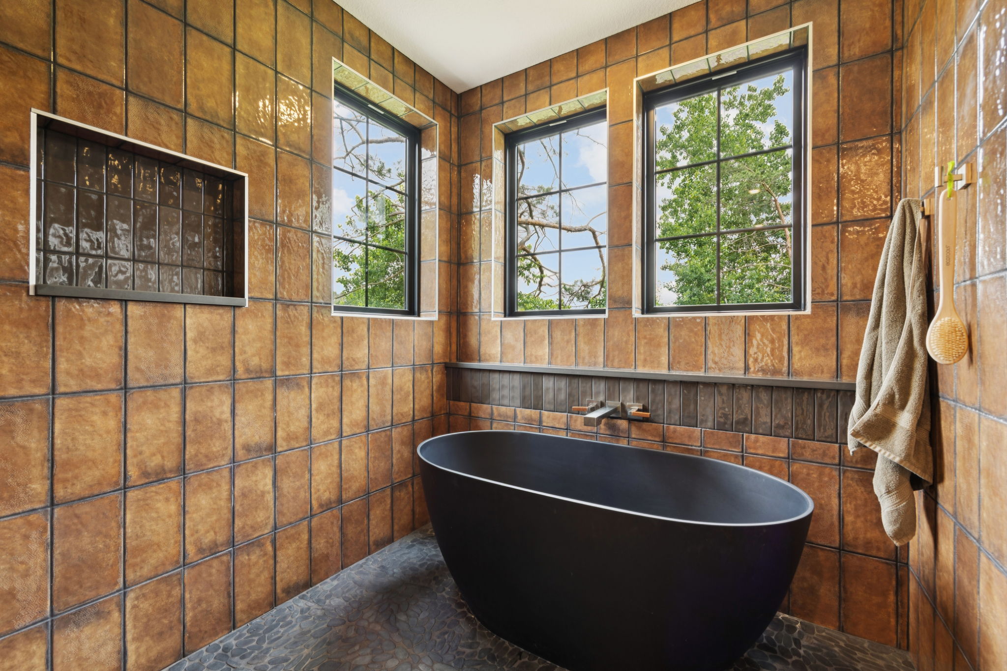 Primary bath with freestanding black soaking tub and amber tile